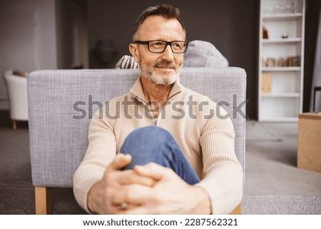 Middle-aged man sitting on living room floor and looking to the side Royalty-Free Stock Photo #2287562321