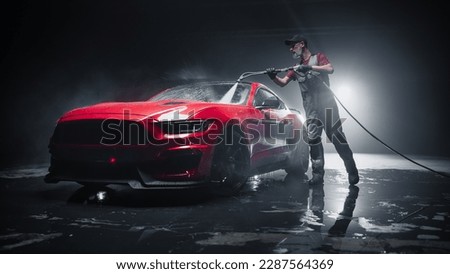 Car Wash Expert Using Water Pressure Washer to Clean a Red Modern Sportscar. Adult Man Washing Away Dirt, Preparing an American Muscle Car for Detailing. Creative Cinematic Photo with Luxury Vehicle Royalty-Free Stock Photo #2287564369