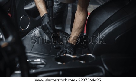 Specialist Professional Car Cleaning and Detailing Company Vacuum Cleaning an Ecological Perforated Black Faux Leather Interior in a Modern Sportscar. Worker Cleaning Every Little Seam on the Car Seat Royalty-Free Stock Photo #2287564495