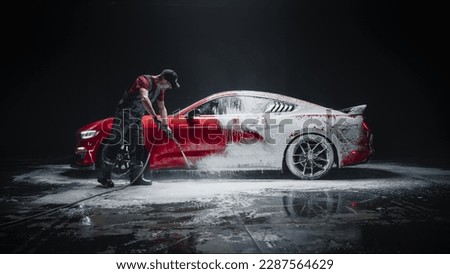Car Wash Specialist Using Pressure Washer to Rinse a Red Modern Sportscar. Adult Man Washing Away Dirt, Preparing a Tuned Car for Detailing. Creative Cinematic Photo in Studio Royalty-Free Stock Photo #2287564629