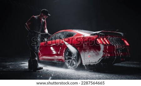 Automotive Detailer Washing Away Smart Soap and Foam with a Water High Pressure Washer. Red Performance Car Getting Care and Treatment at a Professional Vehicle Detailing Shop Royalty-Free Stock Photo #2287564665