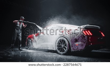 Automotive Detailer Washing Away Smart Soap and Foam with a Water High Pressure Washer. Red Performance Car Getting Care and Treatment at a Professional Vehicle Detailing Shop Royalty-Free Stock Photo #2287564671