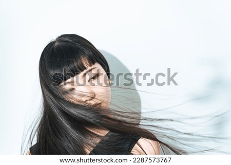 Young Asian girl blowing her long hair. Hair care concept. Royalty-Free Stock Photo #2287573767