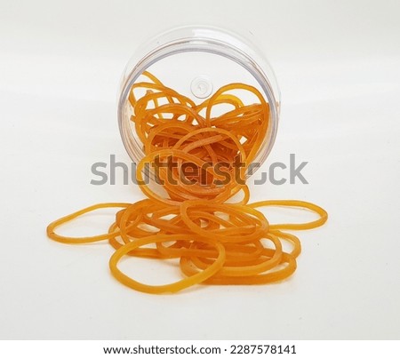 Elastic Golden Rubber Bands Pile coming out of transparent jar on white background.