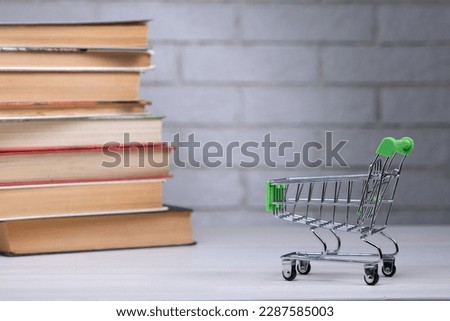 Stack with books and mini shopping cart on table, education concept, tuition fee