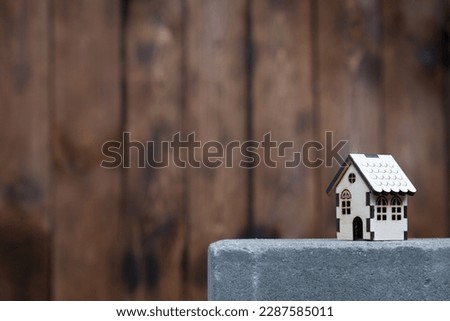 Model of a wooden house with copy space on the left against the background of a wooden wall. The house stands on a concrete slab, the concept of building or buying a home