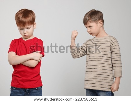 Boy with clenched fist looking at scared kid on light grey background. Children's bullying Royalty-Free Stock Photo #2287585613