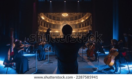 Back View Cinematic shot of Conductor Directing Symphony Orchestra with Performers Playing Violins, Cello and Trumpet on Classic Theatre with Curtain Stage During Music Concert Royalty-Free Stock Photo #2287585941