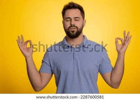 Keep calm down, relax, inner balance. Young caucasian man breathes deeply with mudra gesture, eyes closed, meditating with concentrated thoughts, peaceful mind. Guy isolated on yellow background