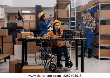 Warehouse employee doing office work in disability friendly workplace. Young asian woman postal service worker in wheelchair checking products stock logistics on laptop in storehouse Royalty-Free Stock Photo #2287605615