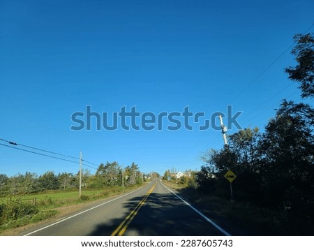 The view of a well cared for stretch of highway under a blue sky. The empty two lane highway is surrounded by vegetation on either side.