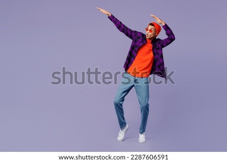 Full body young man of African American ethnicity wear casual shirt orange hat doing dab hip hop dance hands move gesture youth sign isolated on plain pastel purple color background studio portrait Royalty-Free Stock Photo #2287606591