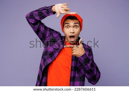 Young shocked fun man of African American ethnicity wear casual shirt orange hat do photographing gesture with hands frame look camera isolated on plain pastel purple color background studio portrait