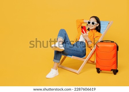 Young fun woman wear summer clothes sit in deckchair use mobile cell phone isolated on plain yellow background. Tourist travel abroad in free spare time rest getaway. Air flight trip journey concept