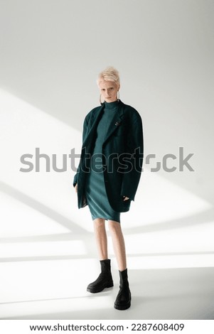 full length of young albino woman with fair-skin posing in green dress and coat on grey background Royalty-Free Stock Photo #2287608409