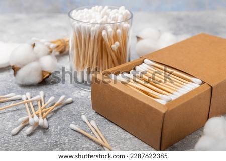 Cotton swabs in craft packaging and holder on a gray cement background. Bamboo cotton buds. Means for hygiene of ears. Eco-friendly materials.Hygienic cotton ear buds.