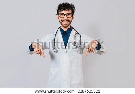 Young doctor pointing a promotion down. Handsome doctor pointing down an isolated advertising space. Happy doctor pointing fingers down