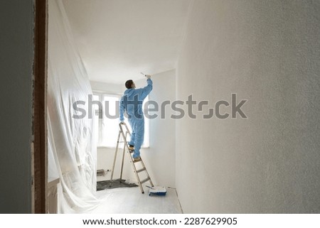 Man stands on the stairs and paints the wall with a roller Royalty-Free Stock Photo #2287629905