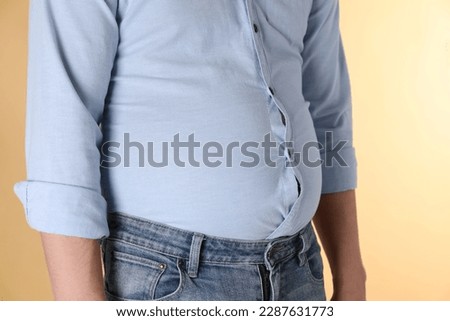 Overweight man in tight shirt on yellow background, closeup Royalty-Free Stock Photo #2287631773