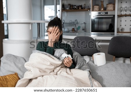 Ill upset young woman sitting on sofa covered with blanket freezing blowing running nose got fever caught cold sneezing in tissue, sick girl having influenza symptoms coughing at home, flu concept Royalty-Free Stock Photo #2287650651