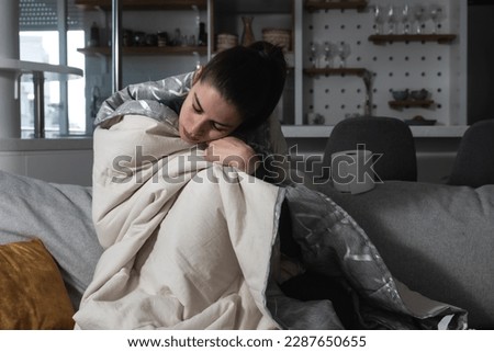 Ill upset young woman sitting on sofa covered with blanket freezing blowing running nose got fever caught cold sneezing in tissue, sick girl having influenza symptoms coughing at home, flu concept Royalty-Free Stock Photo #2287650655