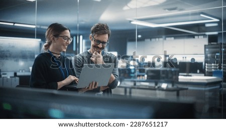 Portrait of Two Creative Young Female and Male Engineers Using Laptop Computer to Analyze and Discuss How to Proceed with the Artificial Intelligence Software. Standing in High Tech Research Office Royalty-Free Stock Photo #2287651217
