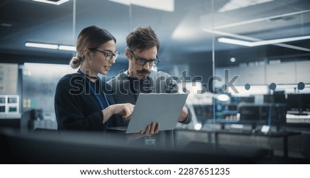 Portrait of Two Creative Young Female and Male Engineers Using Laptop Computer to Analyze and Discuss How to Proceed with the Artificial Intelligence Software. Standing in High Tech Research Office Royalty-Free Stock Photo #2287651235
