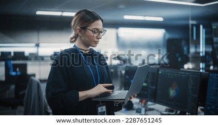 Portrait of a Multiethnic QA Engineer Working on Finding and Fixing Bugs in a Product or Software Before the Launch. Female Using Laptop in a Room with Big Green Screen Mock Up Display Royalty-Free Stock Photo #2287651245