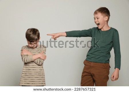 Boy laughing and pointing at upset kid on light grey background. Children's bullying Royalty-Free Stock Photo #2287657321