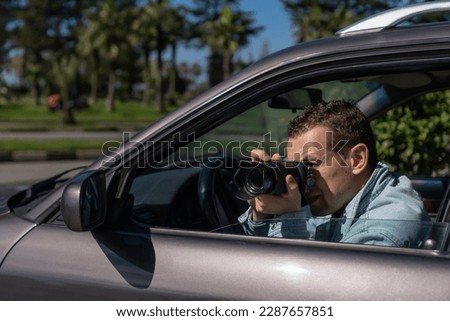 Paparazzi men or guy in sunglasse sits in her car and takes pictures of famous person.Spy with camera in car. Private detective or paparazzi journalist sitting inside car, taking pictures with camera.