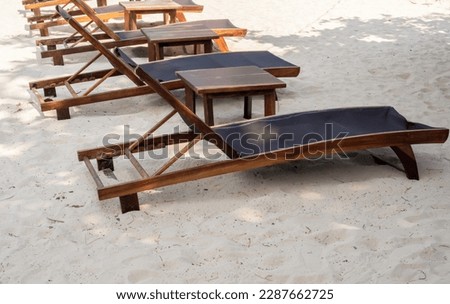 Empty adjustable wooden sunbeds with nobody decoration on sandy beach under the tree on sunny day. Holiday vacation background, summertimes concept.