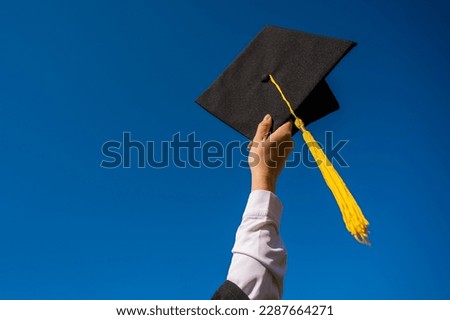 Close-up of a woman's hand with a graduation cap against the blue sky.  Royalty-Free Stock Photo #2287664271