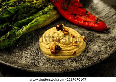 Close-up view of hummus with nuts, grilled vegetables, kale and red pepper, served on a plate in a restaurant