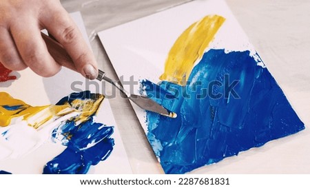 Abstract picture. Painting process. Creative studio. Unrecognizable woman drawing on canvas with spatula and blue yellow paints. Royalty-Free Stock Photo #2287681831