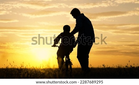 Father helps his daughter ride bike. Father teaching little daughter to ride bike in park. Child rides bike. Child, dad play together, sunset. Chidhood dream. Kid Girl learns to ride bike.Happy family Royalty-Free Stock Photo #2287689295