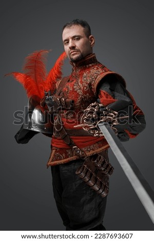 Shot of medieval musketeer swordsman with epee and helmet against gray background.