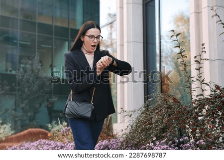 Emotional woman checking time on watch outdoors. Being late concept Royalty-Free Stock Photo #2287698787