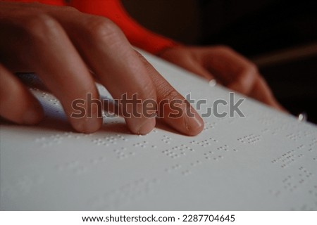 A blind woman uses her hand to read music notation in a braille book filled with sheet music.