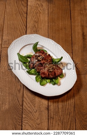 Pork steak on the bone grilled with lettuce. The food lies on a light, oval plate.