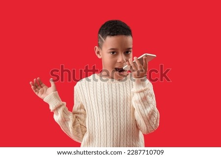 Little African-American boy talking by phone on red background