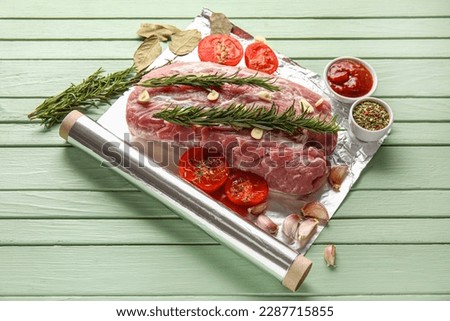 Aluminium foil roll with piece of raw meat, tomatoes, rosemary and spices on color wooden background Royalty-Free Stock Photo #2287715855