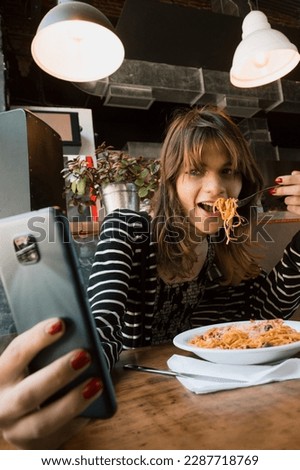 vertical image of transgender young latin woman of argentinian ethnicity eating spaghetti inside a restaurant and taking a selfie