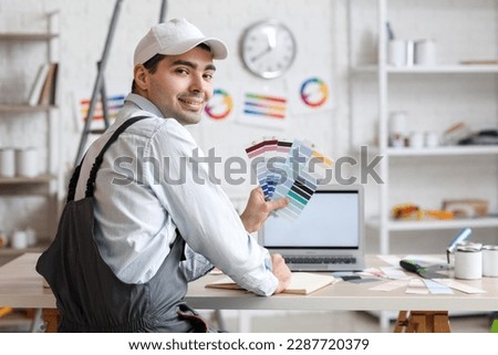 Male painter with color palettes working with laptop at table