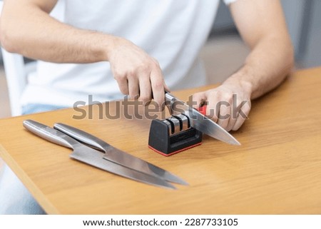 Close-up photo of man sharpening knives with special knife sharpener at home Royalty-Free Stock Photo #2287733105