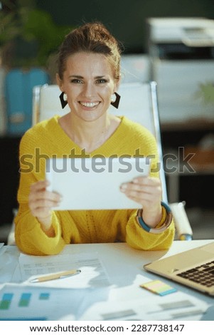 smiling modern small business owner woman in yellow sweater in the modern green office using tablet PC.