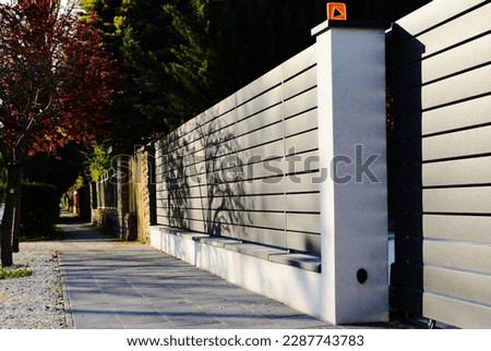 gray metal fence and gate. horizontal panels and gaps.  powder coated finish. diminishing perspective view. modern fence design concept. asphalt sidewalk. white stucco vase and fence piers Royalty-Free Stock Photo #2287743783