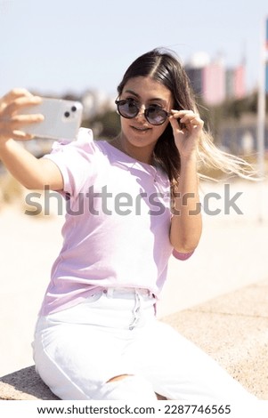 Teen girl taking a selfie on the Rambla in Montevideo. He lowers his dark glasses to pose