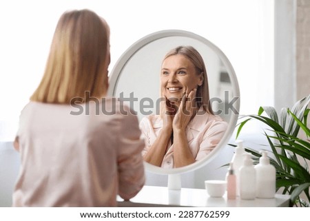 Mature Beauty. Portrait Of Attractive Middle Aged Lady Smiling To Her Reflection In Mirror, Beautiful Woman Enjoying Her Appearance While Making Skincare Routine At Home, Selective Focus Royalty-Free Stock Photo #2287762599