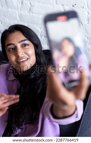 Queer Pakistani Asian Woman taking a selfie with a smartphone by waving at the camera