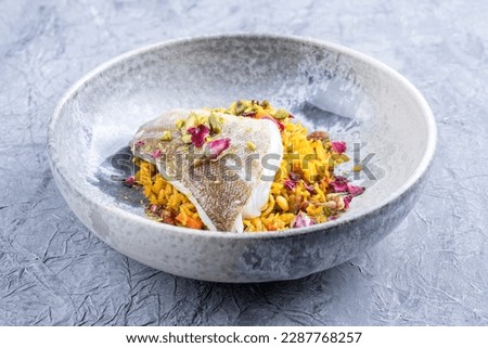Modern style traditional sauteed skrei cod fish filet with skin in a bed of Persian jeweled saffron rice pilaw served in ceramic design bowl as close-up 